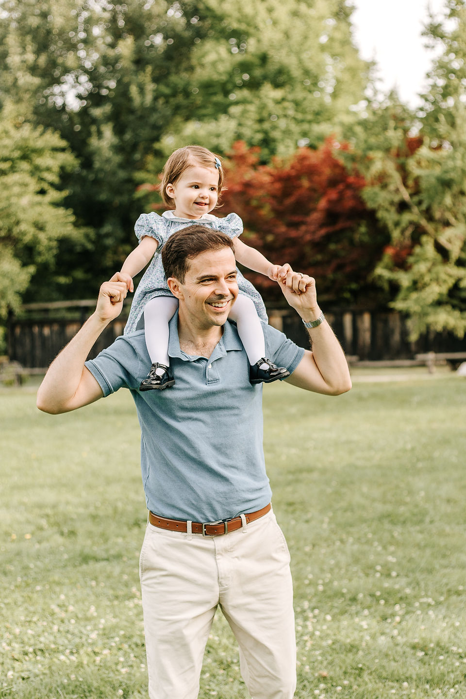a man stands on a grassy field as he holds a young girl on his shoulders