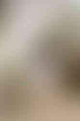 A girl sits on a small wooden bench and smiles as she is surrounded by a large floral arrangement