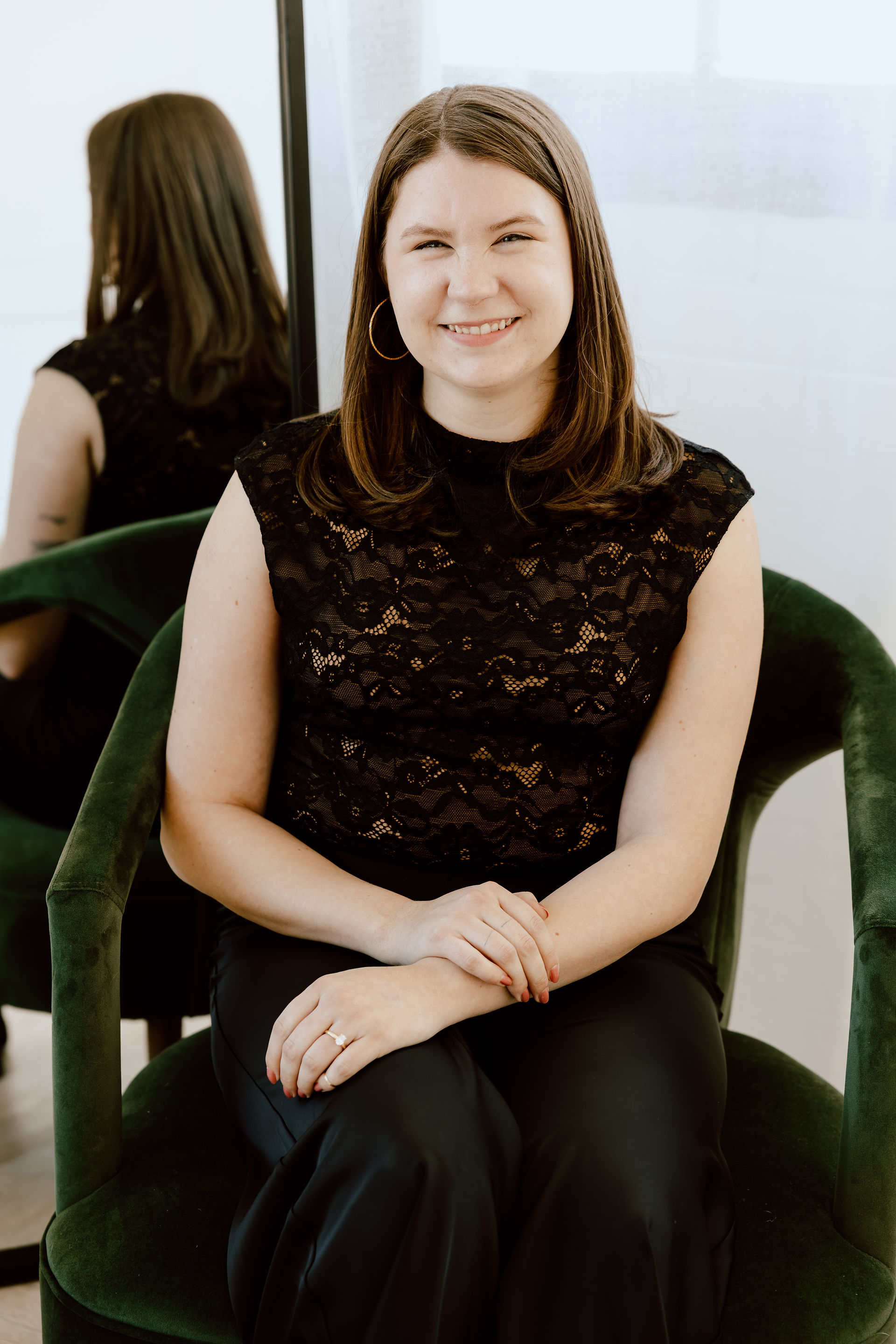 A woman smiles as she sits in a green velvet chair
