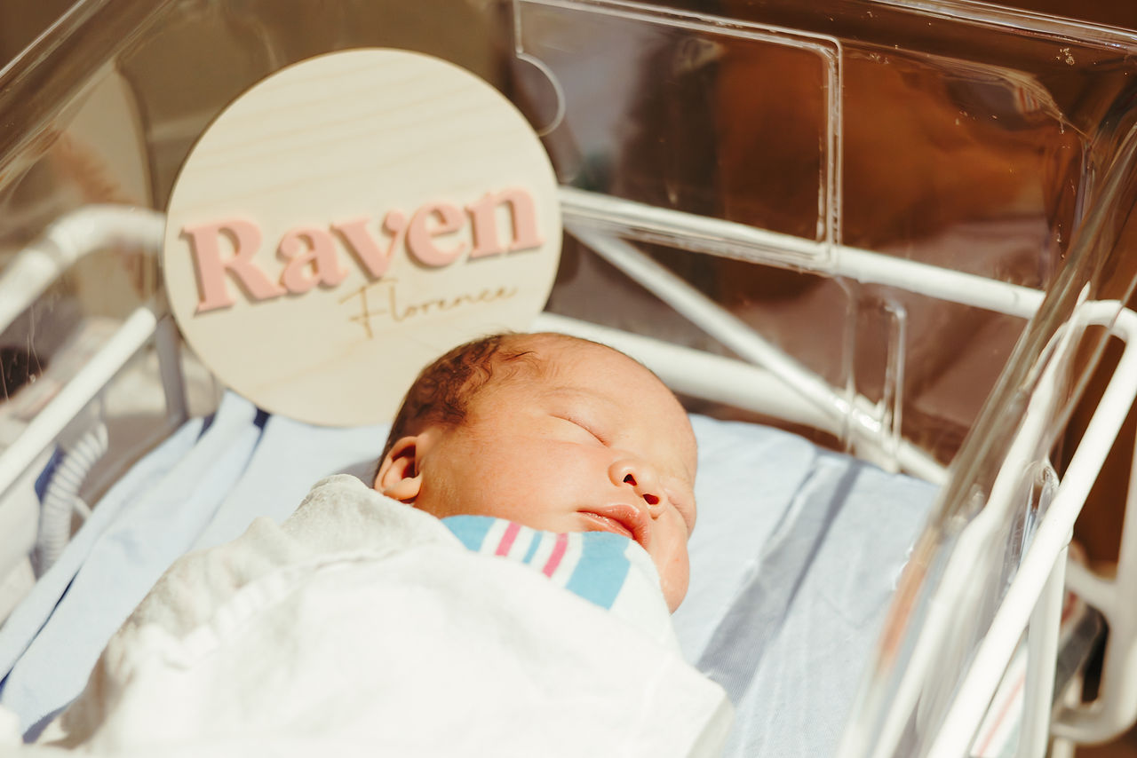 A newborn baby wrapped in a hospital blanket lies in a bassinet and sleeps