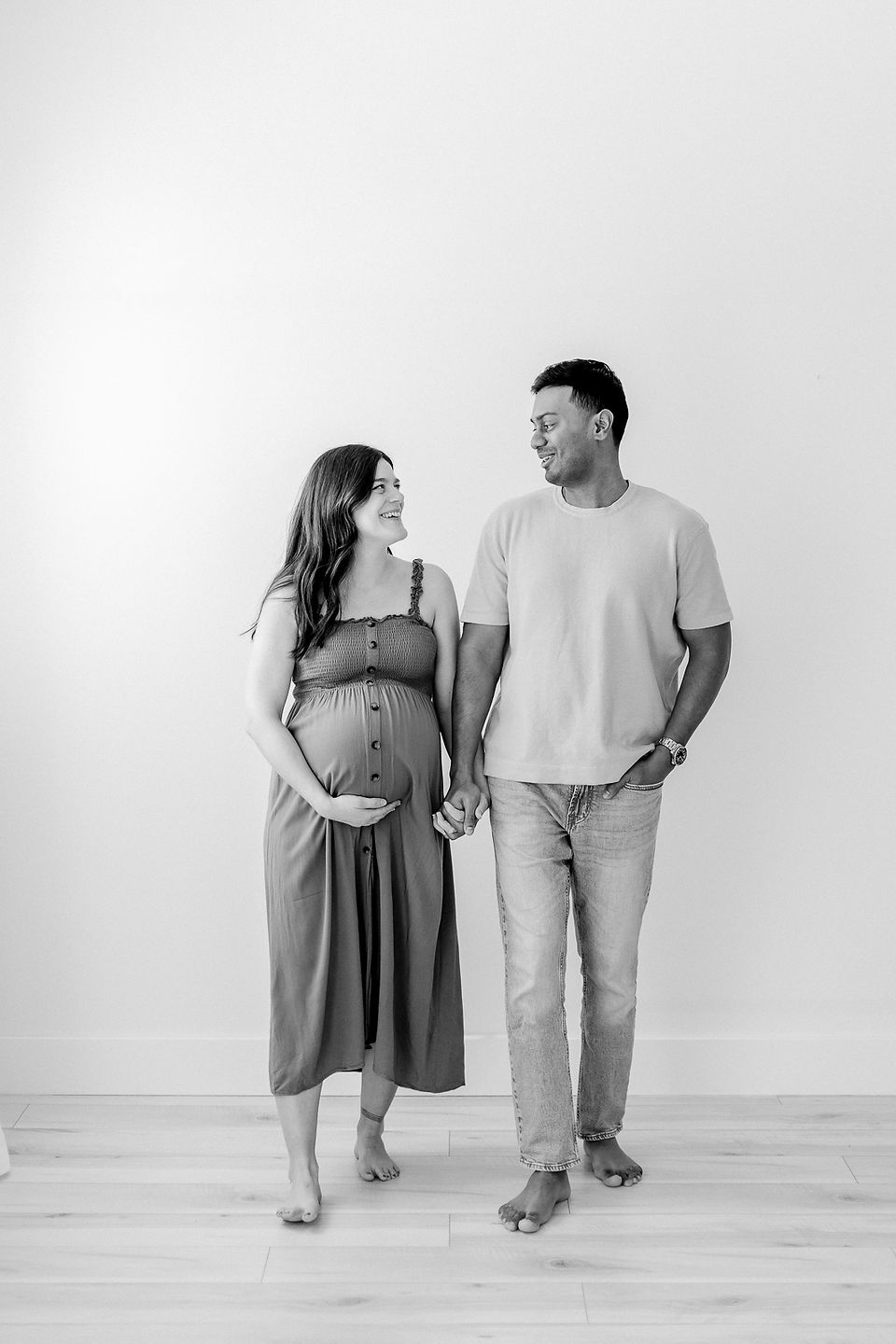 black and white image of a couple walking and looking at each other as the woman cradles her pregnant stomach