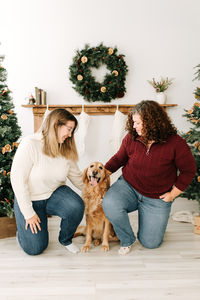 Two woman kneel and look down at the golden retreiver dog sitting between them
