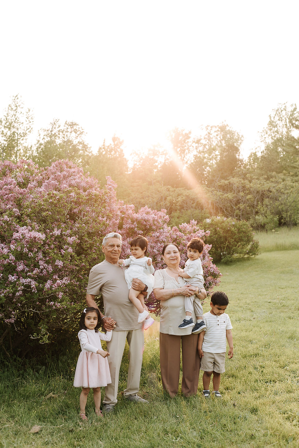 Two grandparents stand by a lilac bush with their 4 grandchildren