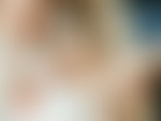 A baby lies in a bassinet and holds onto the fingers of a man and woman