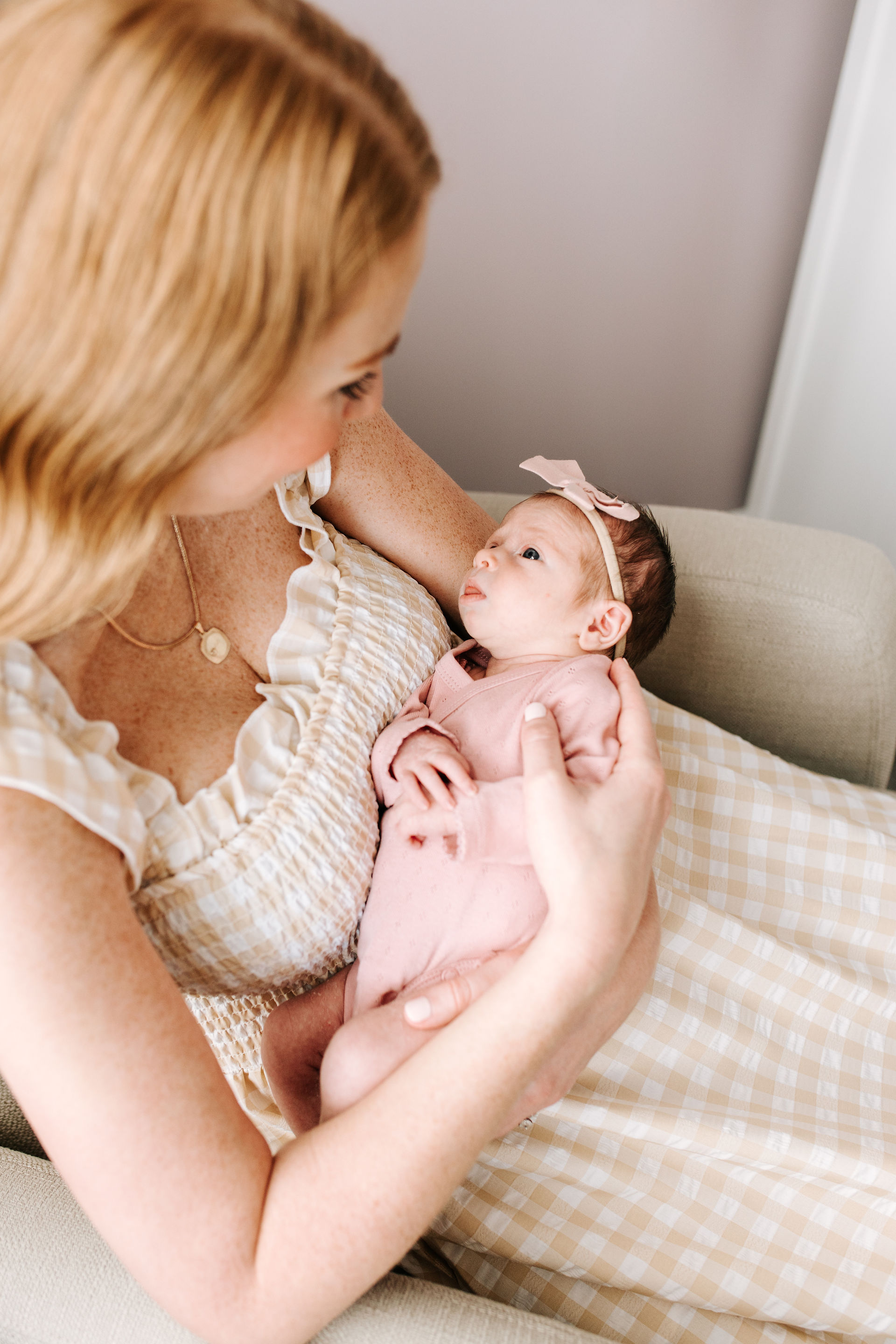 a woman sits and cradles a baby in a pink outfit and bow while looking down at her