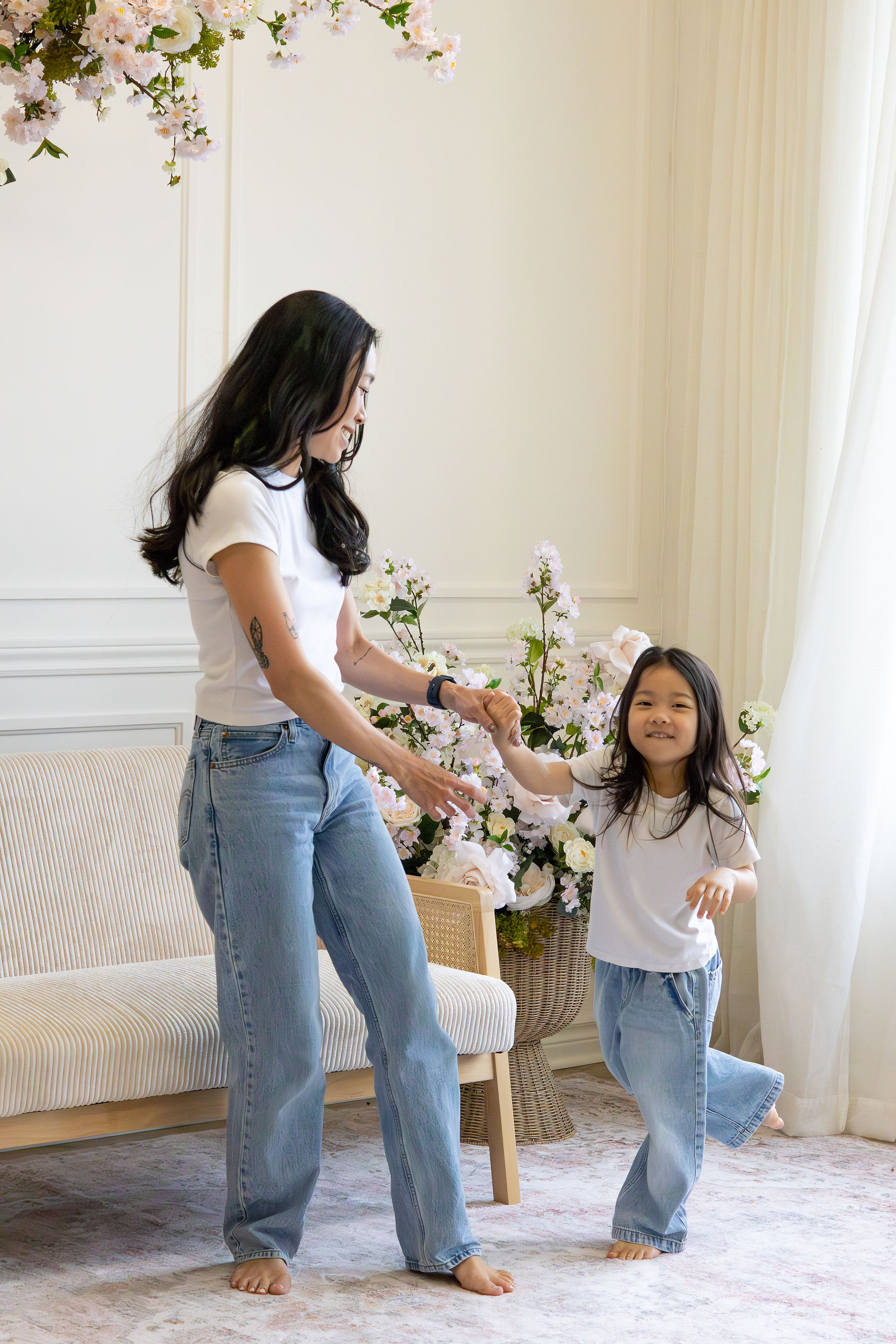 A woman in jeans and a white t shirt dances with a young girl also in jeans and a white t shirt