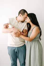 A man and woman stand and rest their foreheads together as the man holds a newborn baby in his arms