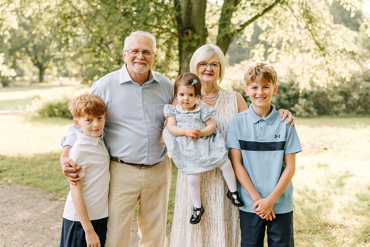 An older man and woman stand with two young boys and a young girl under a tree