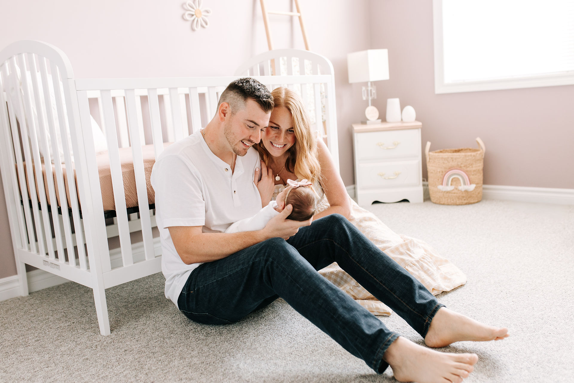 a man and woman sit on the floor of a nursery and hold a baby while looking down at her