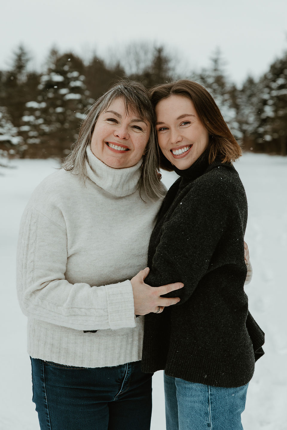 A young woman and older woman hug and smile outside in the snow