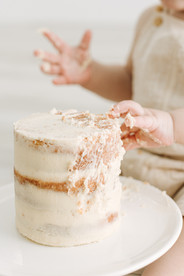 white cake on cake stand with baby's hands grabbing it