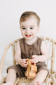 A young boy sits in a small rattan chair and holds a toy while smiling