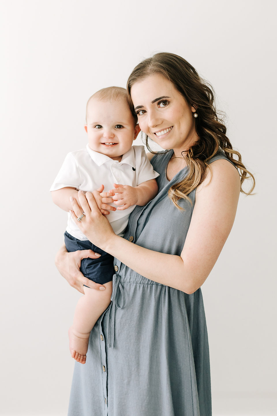 A woman holds a one year old boy in her arms and they both smile