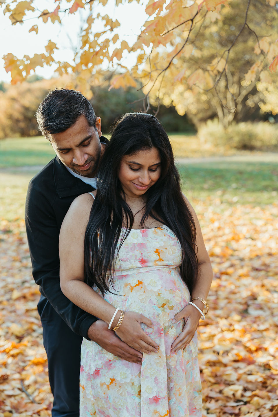 A woman cradles her pregnant stomach as a man stands behind her and rests his hands on her stomach