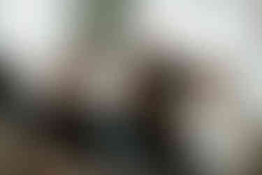 An older couple sit on a couch as three young adult children sit on the floor in front of them