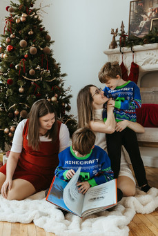 Two woman and two boys sit on a blanket in front of a Christmas tree