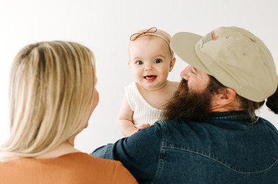Th back of a man and woman's head as they next to each other and hold a one year old girl up between them