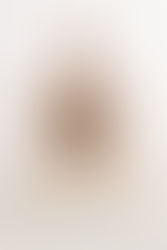 A young boy sits in a small rattan chair and holds a toy while smiling