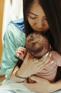 A woman in a hospital gown kisses the forehead of a newborn baby