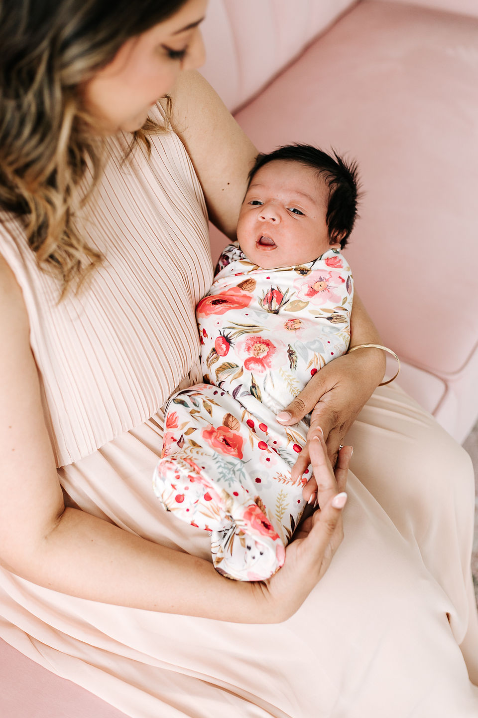over the head shot of woman sitting on a couch while she looks down and holds a newborn baby in a swaddle