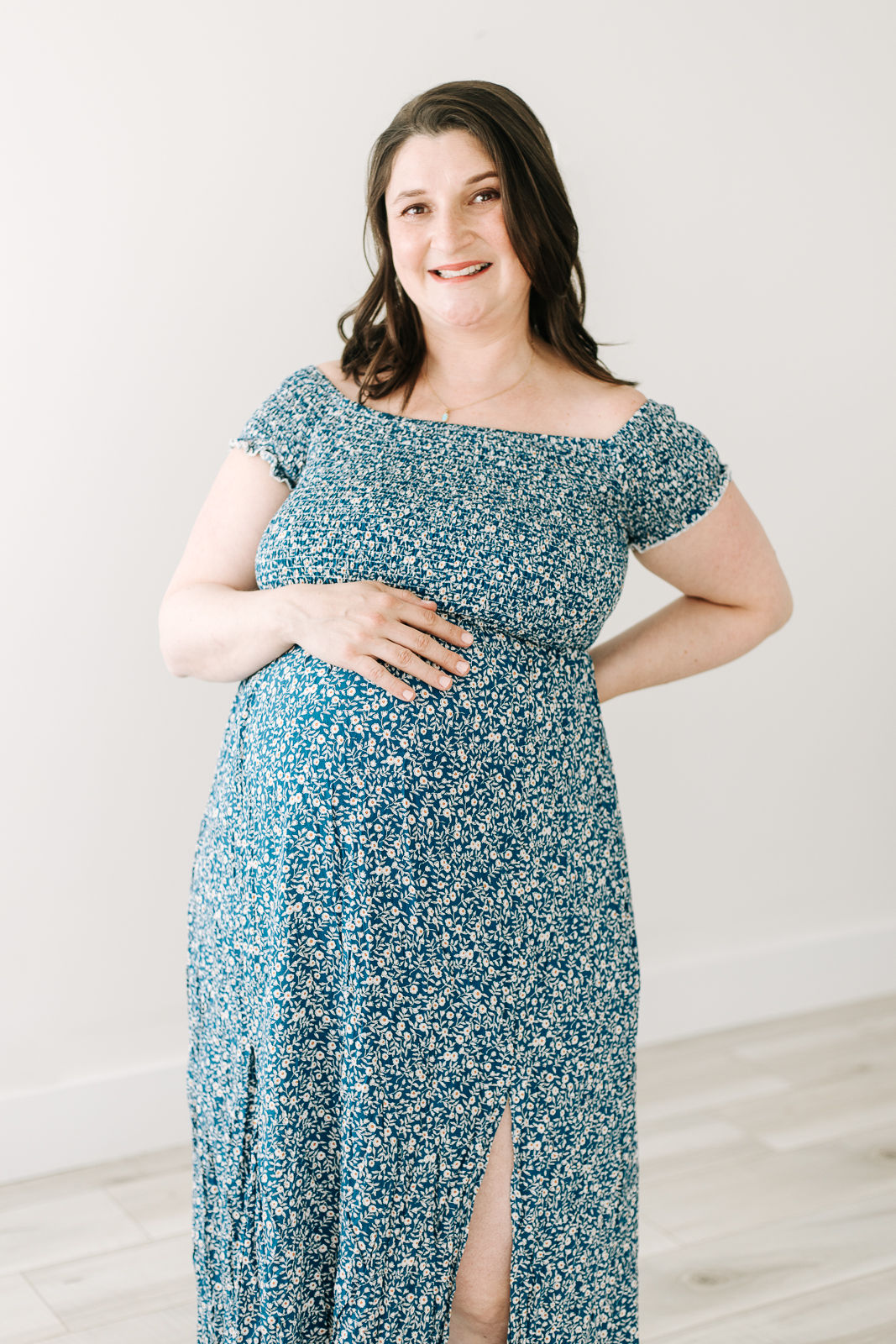 A pregnant woman in a blue floral dress stands with one hand resting on her stomach