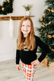 A girl in pajamas stands in front of a Christmas tree