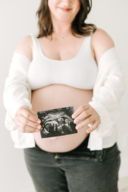 torso of a pregnant woman in a white button down shirt and white bra holding an ultrasound photo