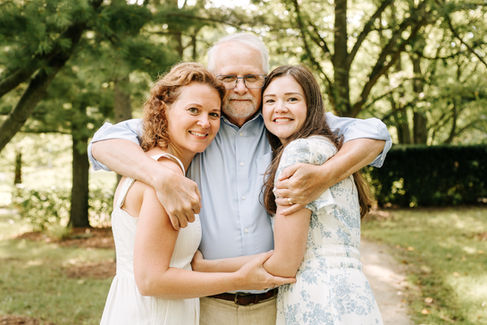 An older man has his arms around the shoulders of two woman who hug him