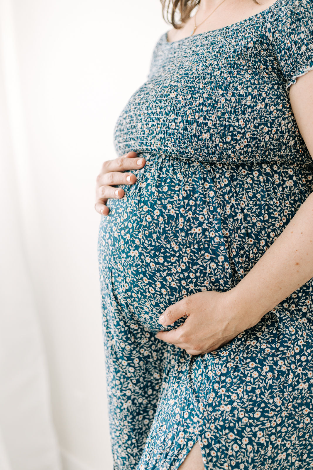 torso profile of a pregnant woman in a blue floral dress resting her hands on her stomach
