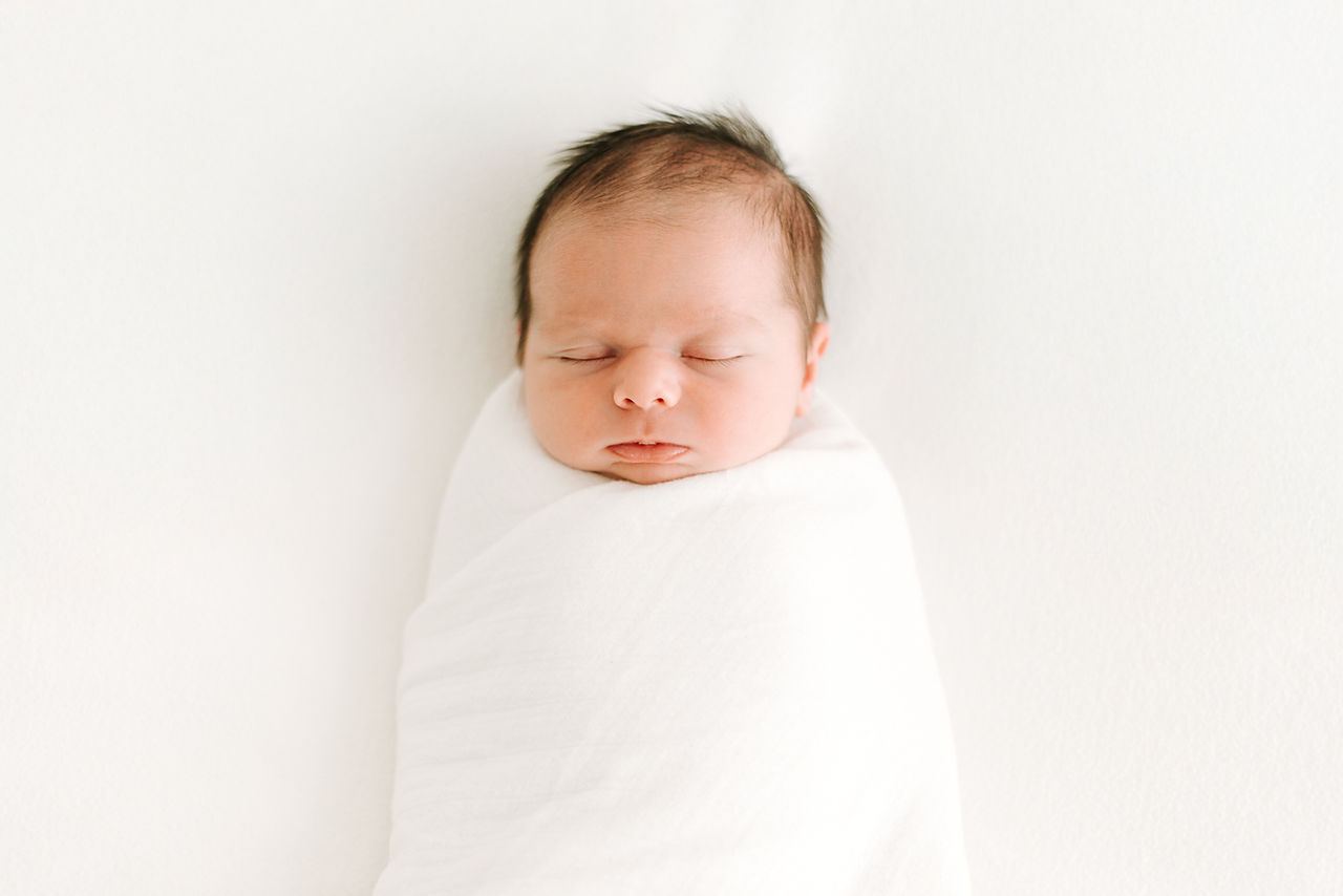 A newborn baby swaddled in a white blanket