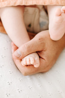 A man's hand holds a baby's foot