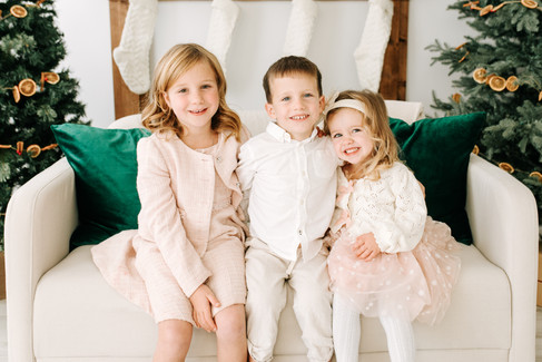 Three kids sit on a couch in between two Christmas trees