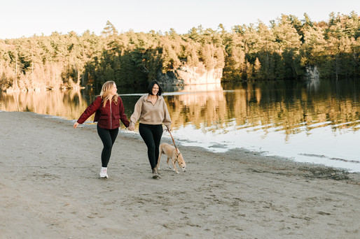 Two woman run with a dog on a leash on a beach by a lake