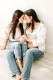 two woman sit on the floor with their foreheads touching, hugging and one pair of legs on top of the other