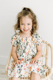 A toddler girl sits on a small rattan chair