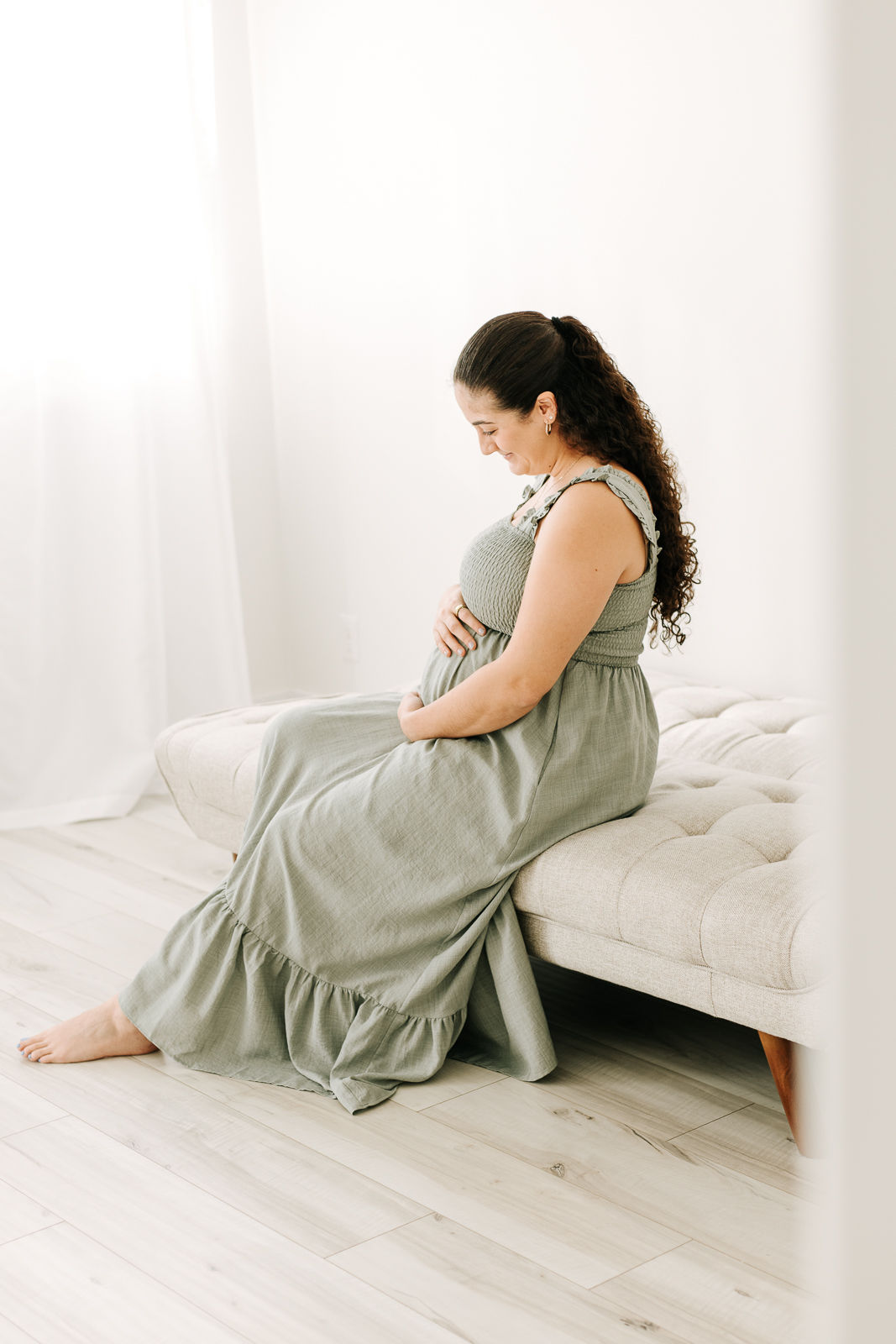 pregnant woman sitting on the edge of a couch holding her pregnant stomach and looking down at it