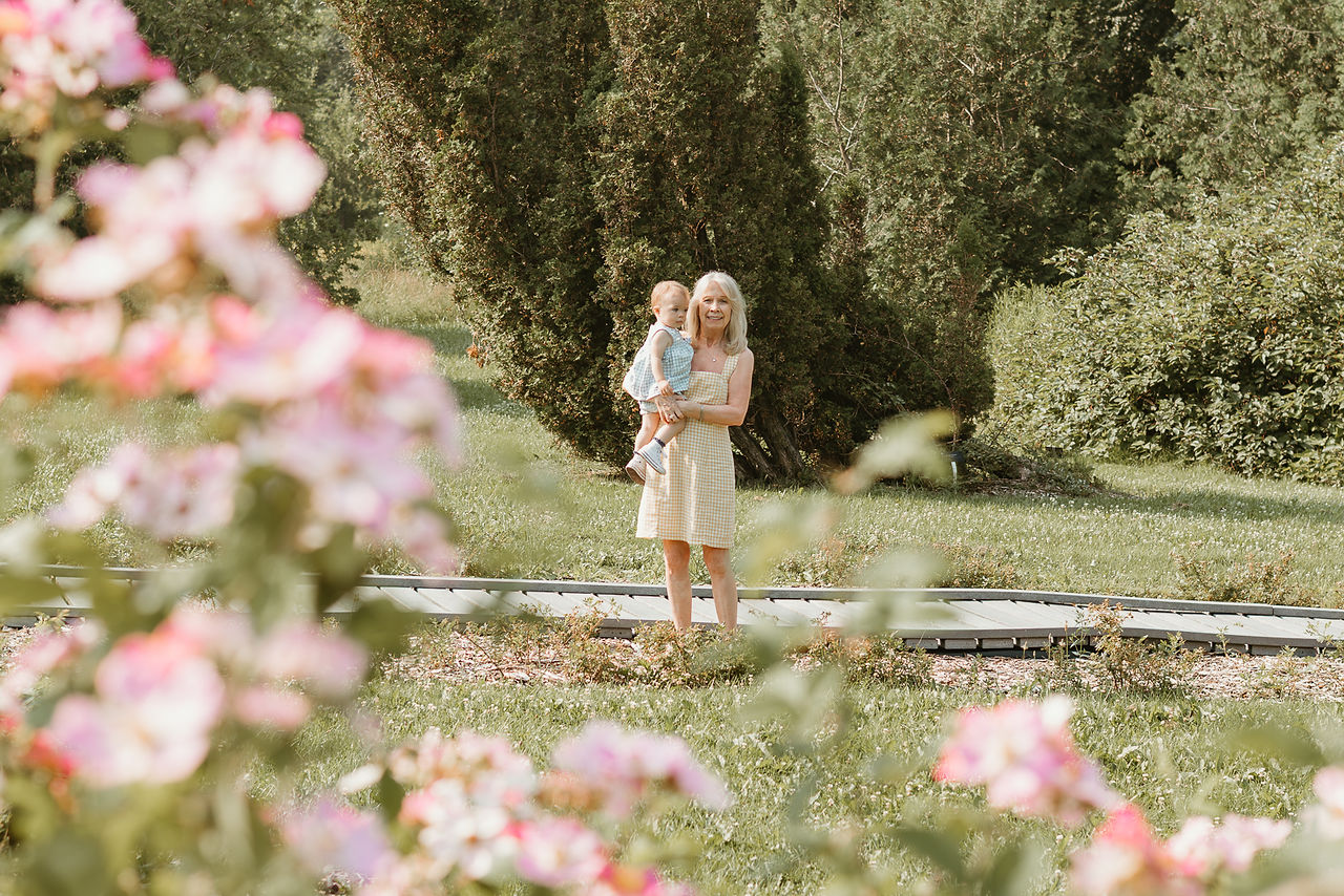 An older woman holds a one year old girl in a garden