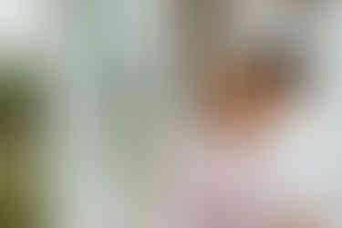 A man kisses the cheek of a woman as they stand in the doorway of a whote greenhouse