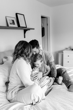 black and white image of a family of four on a bed looking down at a newborn baby