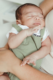 A newborn baby in a white onesie and green overalls