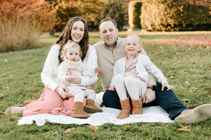 A couple and two young girls sit on a blanket on the grass in fall