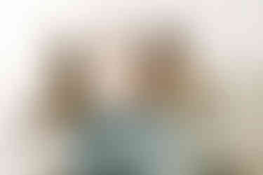 A woman sits beside a man on a couch while he holds a newborn baby in his arms and a dog sits on the other side of him