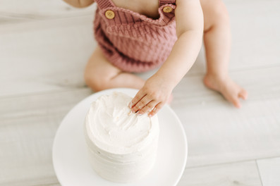 A one year old plays with a small white cake on a cake stand