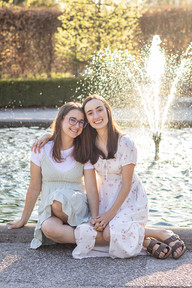 Two woman sit in front of a fountain and hold hands