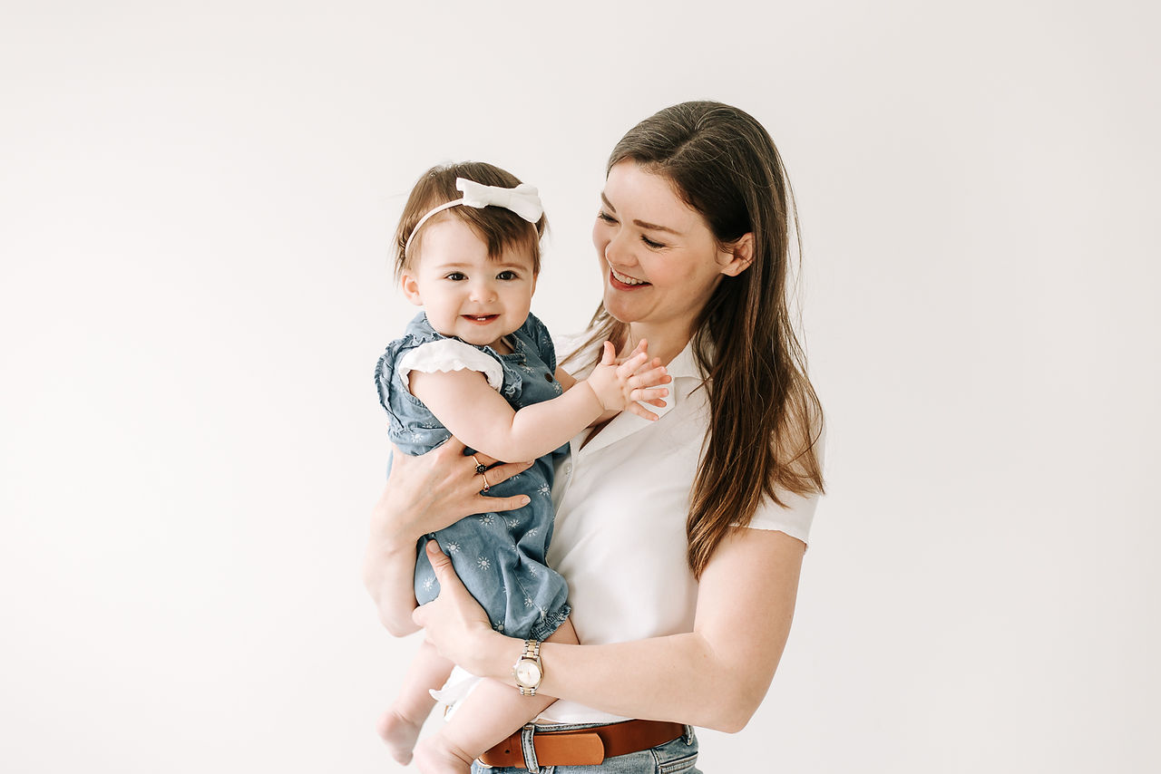 A woman holds a one year old girl in her arms and looks down at her