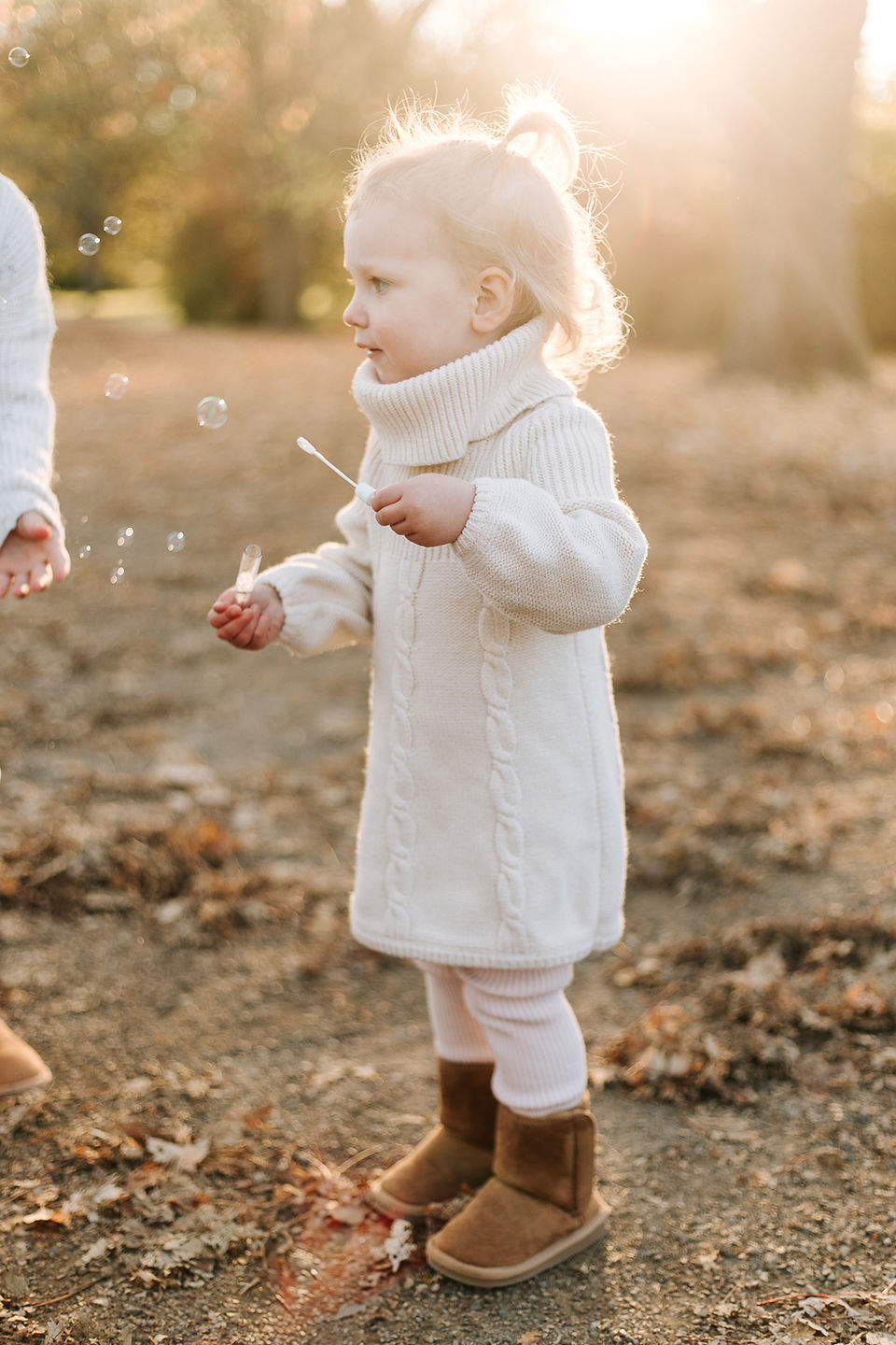 A little girl blows bubbles as she stands under a tree in fall