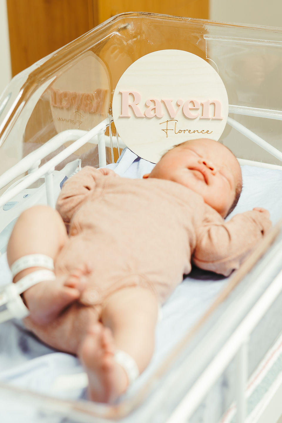 A newborn baby in a pink onesie lies in a bassinet and sleeps