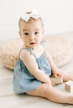 A six month old girl sits on the floor and plays with wooden blocks