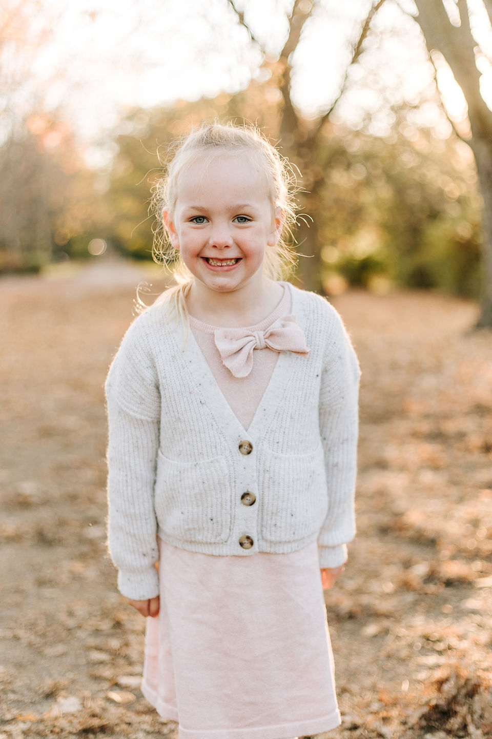 A young girl smiles as she stands under trees in the fall as the sun sets