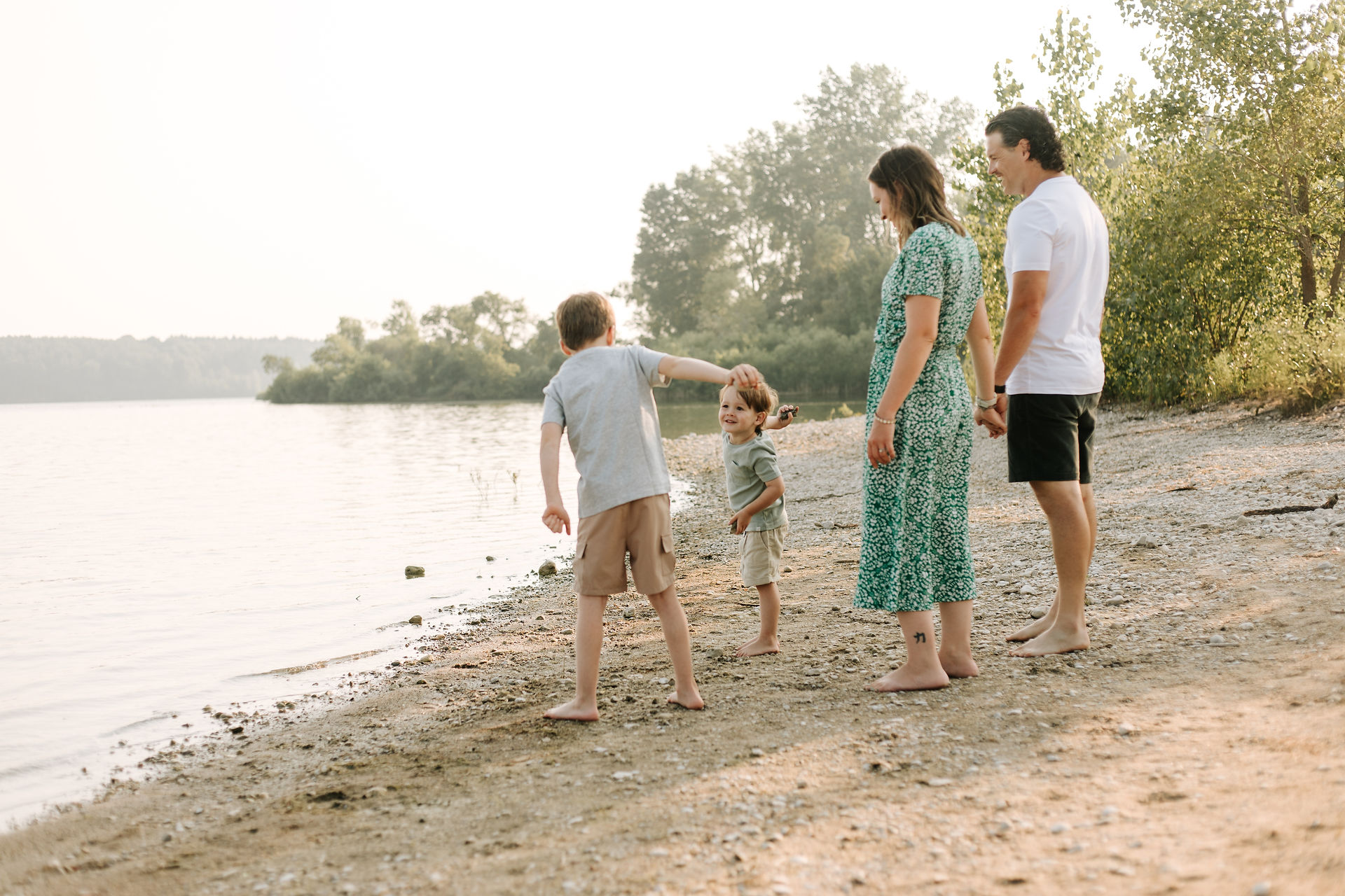 Two young boys throw rocks into a lake as a woman and man watch them